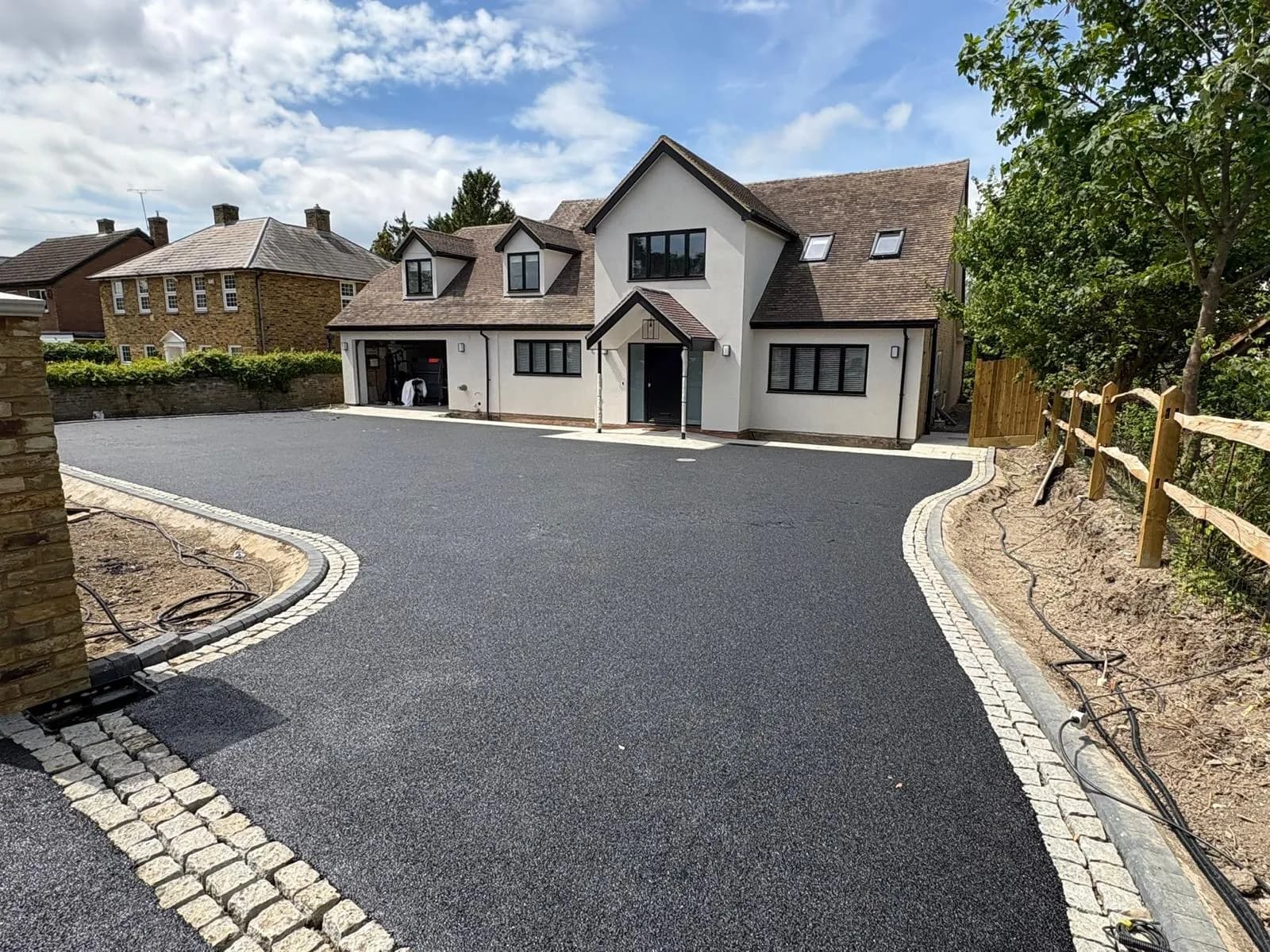 Curved black-surfaced driveway beside a white house with stone edging