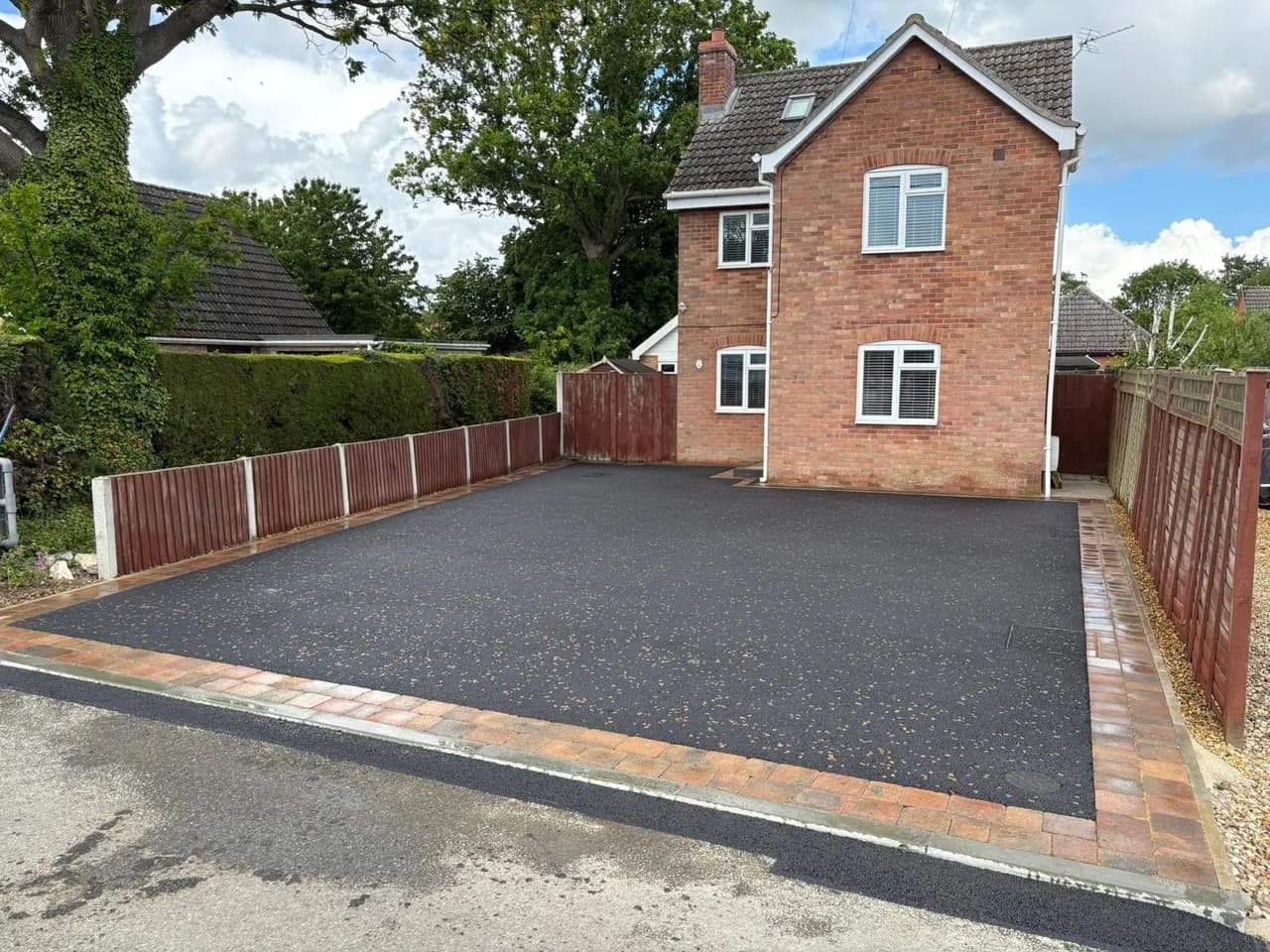 Angled view of a finished black-surfaced driveway at a brick house