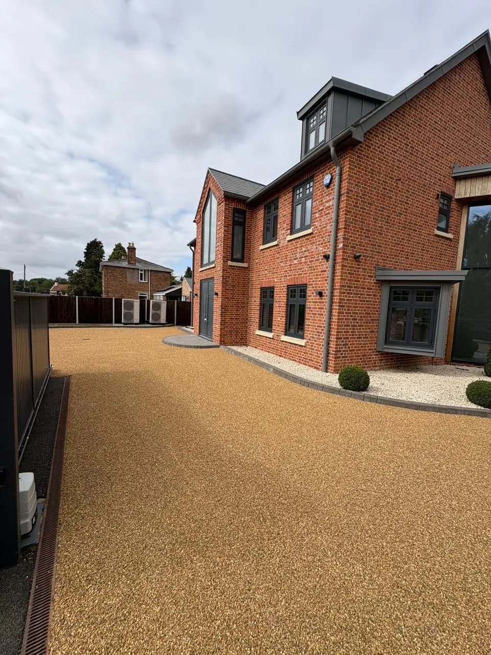 Golden stone driveway beside a brick house with edging and a drainage channel