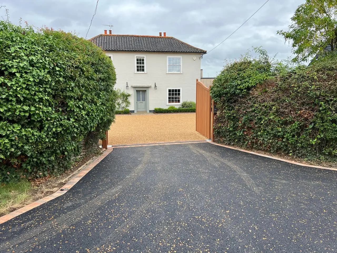 Black entrance apron and golden stone driveway beyond timber gates