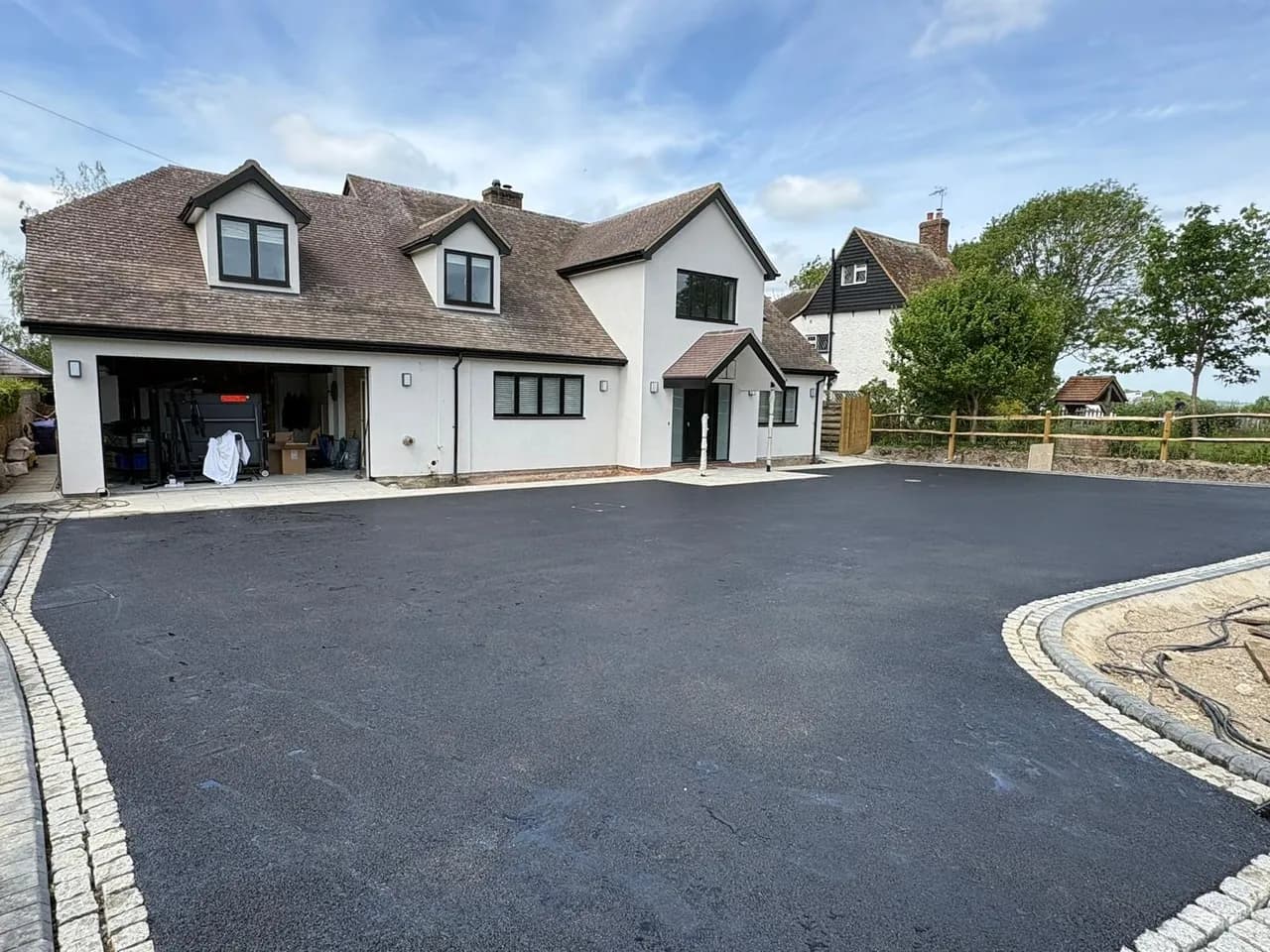Wide black-surfaced driveway alongside a white house