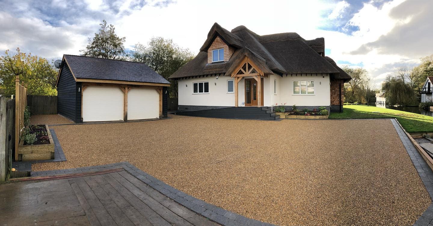 Gravel driveway in front of a thatched cottage and double garage